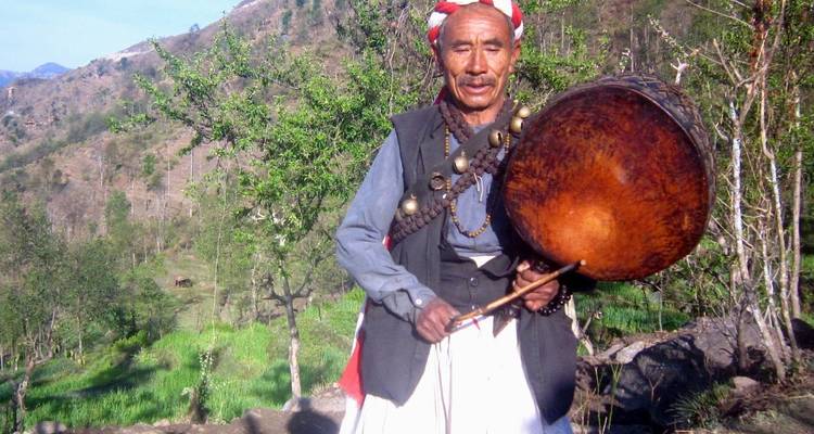 Mann in traditioneller Kleidung mit einer Trommel in einer ländlichen Landschaft.
