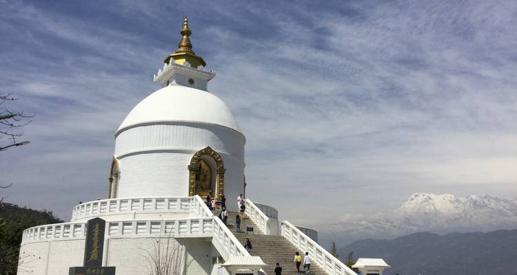 Witte pagode met mensen die de trap beklimmen, bergen op de achtergrond.