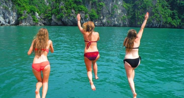 Drie vrouwen in zwempakken die in helder blauw water springen.