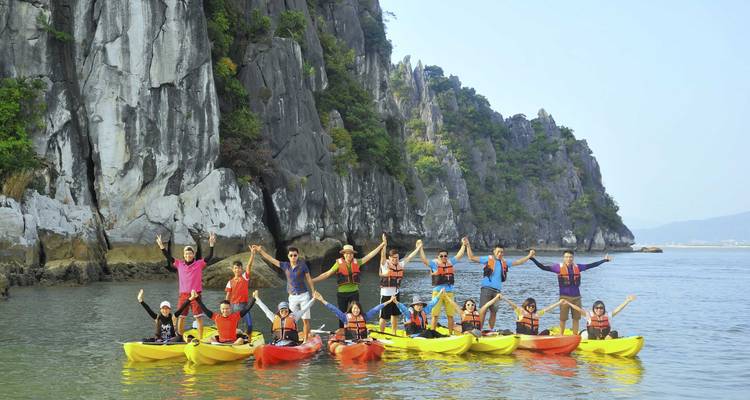 Een groep mensen in kajaks die hun peddels omhoog steken voor rotsachtige kliffen.