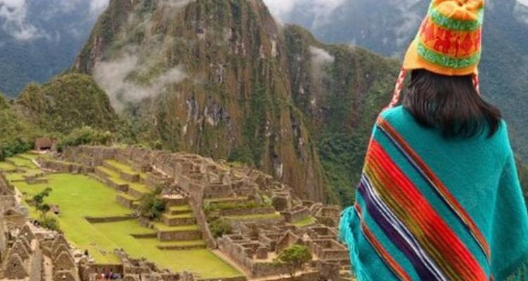 Eine bunte, in einen Poncho gehüllte Person, die die Ruinen von Machu Picchu überblickt.