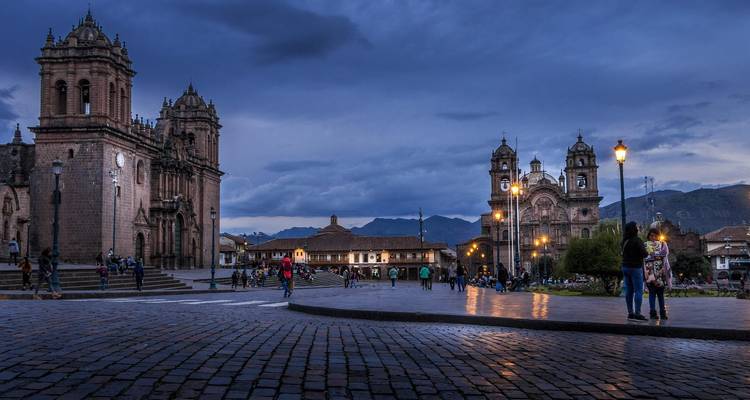 Ein historischer Platz in Cusco, Peru, der bei Abenddämmerung beleuchtet ist, während Menschen umherwandeln.