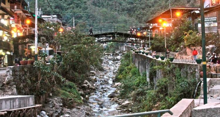 Menschen, die eine Straße entlang gehen mit einem Fluss und einer Brücke, umgeben von Grün.