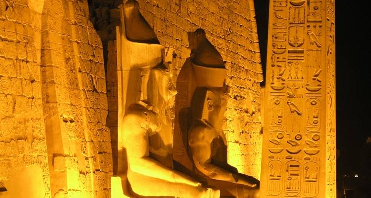 Beleuchtete antike Statuen und Hieroglyphen bei Nacht.