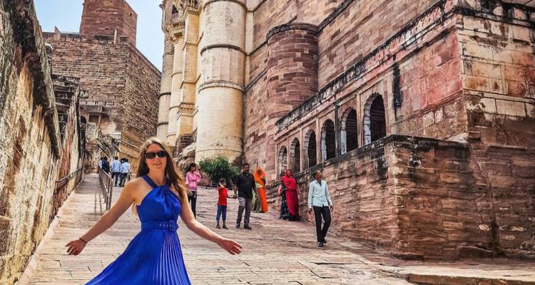 Frau in blauem Kleid vor einer Festung mit Menschen im Hintergrund