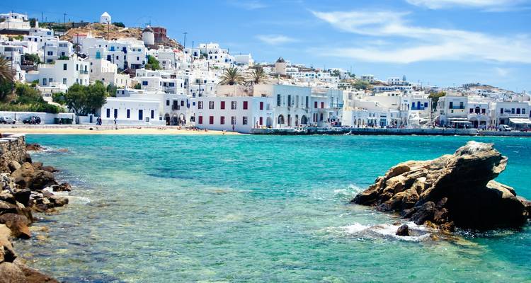 Clear waters with coastal white buildings and a rocky beach.