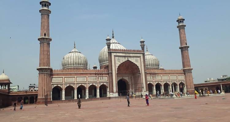 Eine große Moschee mit drei Kuppeln und zwei Minaretten, mit Menschen im Innenhof.