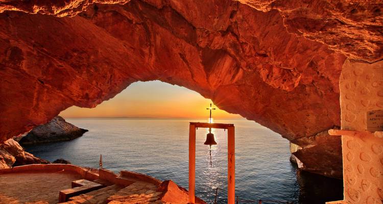 Vista del atardecer a través de la abertura de una cueva con una campana y el mar.