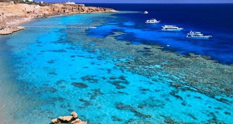 Clear ocean with coral reefs and boats in the distance.