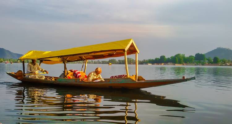 Bateau traditionnel sur un lac calme avec des montagnes en arrière-plan.