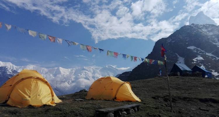 Zeltplatz mit Zelten und Gebetsfahnen vor Bergkulisse.