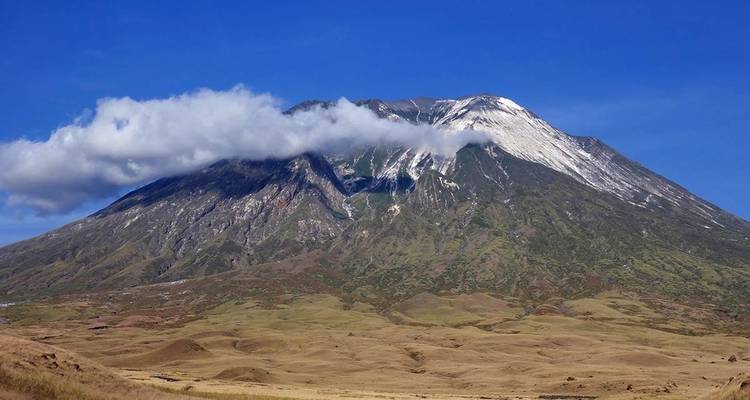 Berg met wolken die zijn top raken onder een levendige blauwe hemel.