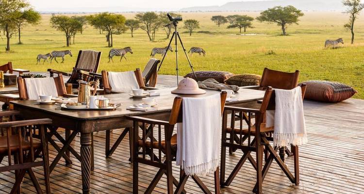 Wooden deck with dining setup overlooking zebras on a savannah.