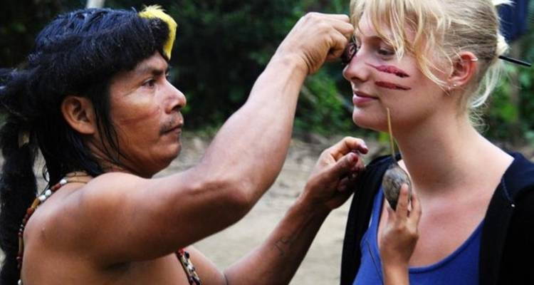 Einheimische Person malt Linien auf das Gesicht eines Besuchers in einer Außenumgebung.
