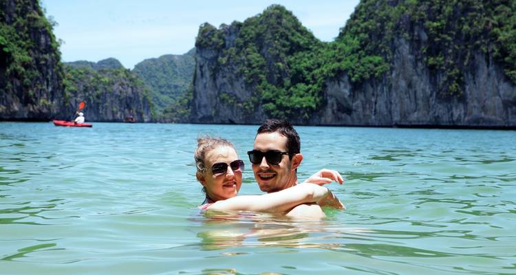 Couple qui s'enlace dans l'eau avec des falaises au loin.