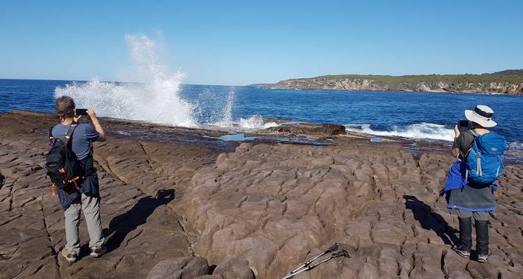 Menschen, die Wellen fotografieren, die sich an der felsigen Küste brechen.