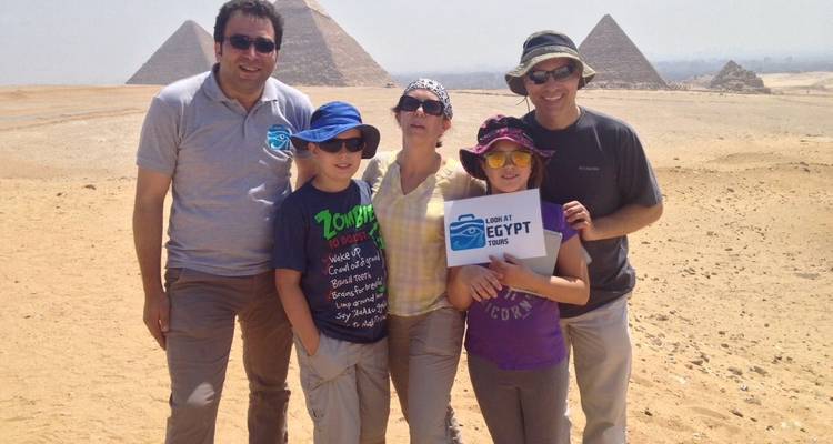 Family posing with a tour sign in front of pyramids.