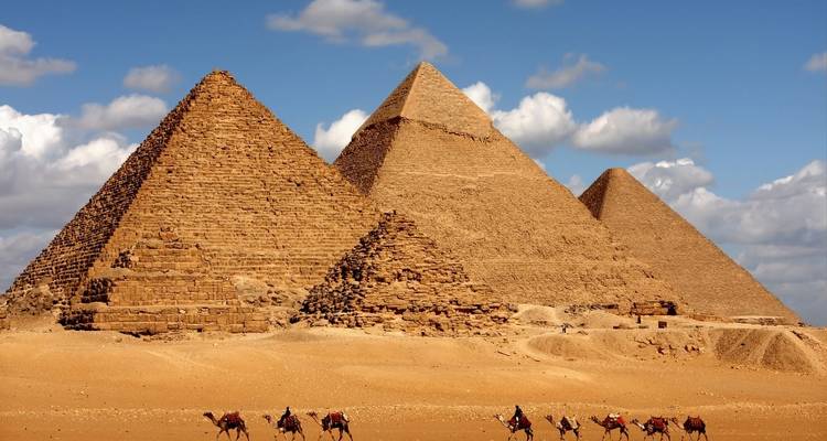 Three pyramids in the desert with camels in the foreground.