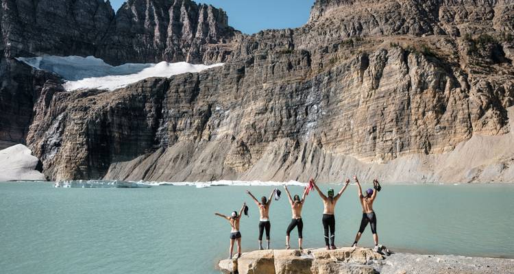 Groupe de personnes célébrant au bord d'un lac turquoise avec des montagnes.