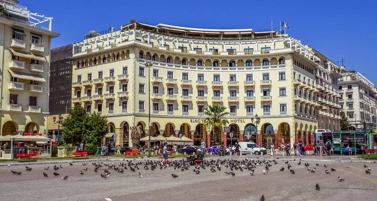 Pigeons et personnes devant l'Electra Palace Hotel pendant la journée.