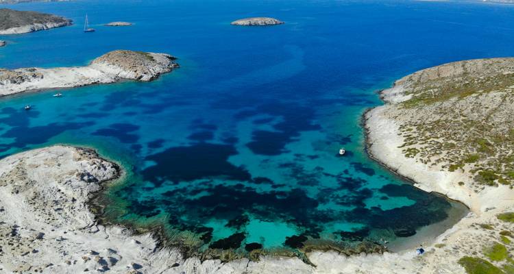 Vista aérea de una cala turquesa apartada rodeada de costa rocosa blanca y mar azul profundo.