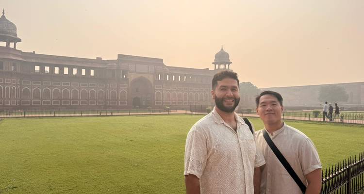 Two men standing in front of a large historic fort in a hazy setting.