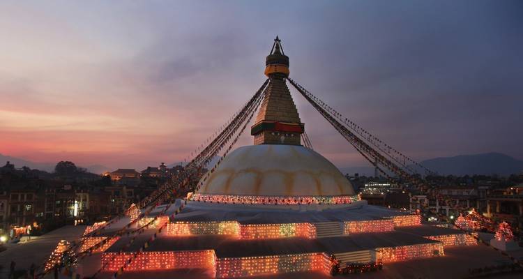 Large stupa decorated with colorful lights at dusk.