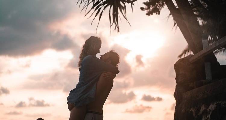 Paar, das sich auf einem Felsen am Meer während des Sonnenuntergangs umarmt.