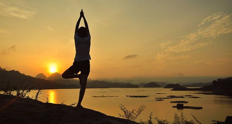 Person, die bei Sonnenuntergang Yoga am See macht.