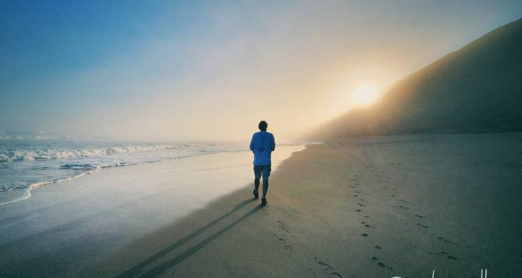 Persona caminando por una playa al atardecer.