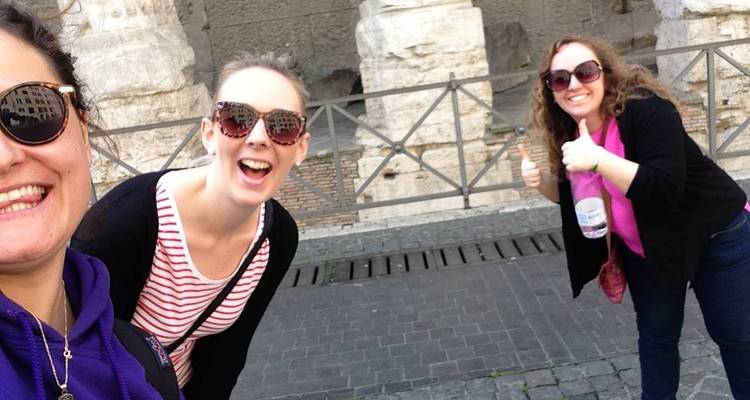 Trois femmes souriantes devant d'anciennes structures de pierre.