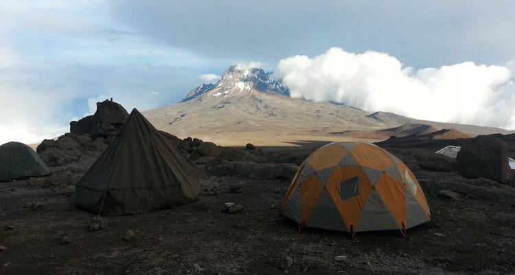 Tenten opgezet aan de voet van een berg met bewolkte luchten.
