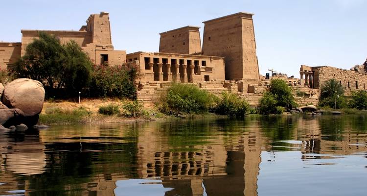 Templo antiguo junto al río con árboles y cielo despejado.