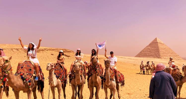 Touristes sur des chameaux avec les pyramides en arrière-plan.