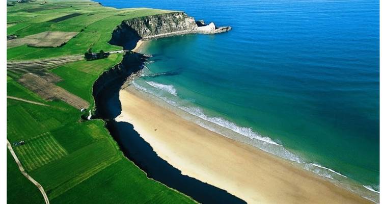 Vista aérea de una playa con acantilados y campos verdes.