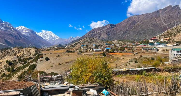 Hooggelegen plateaudorpje met droog landschap omgeven door besneeuwde Himalaya-pieken.