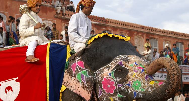 Éléphant décoré avec deux personnes en tenue traditionnelle lors d'un événement culturel.