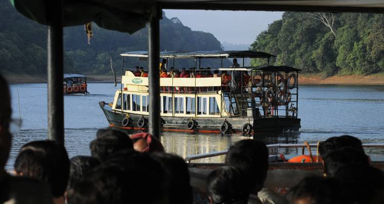 Touristenboote auf einem See mit Menschen an Bord und bewaldeten Hügeln im Hintergrund.
