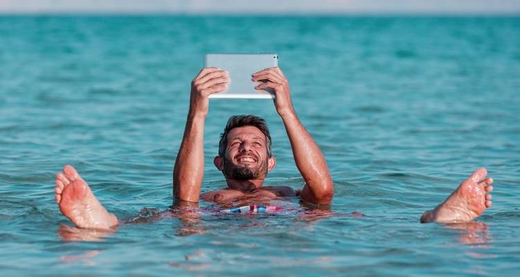 Persona flotando en el agua, sosteniendo una tableta en el Mar Muerto.