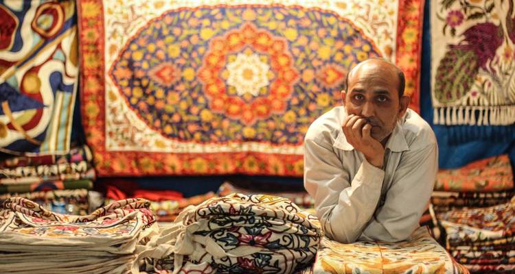 Mann posiert mit Textilien und einem bunten Wandteppich.