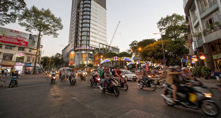 Intersección de ciudad concurrida con motos y edificios modernos altos al atardecer