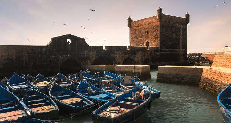 Flota de icónicos barcos de pesca azules amarrados junto a la fortaleza de piedra Skala de la Ville en el puerto de Essaouira