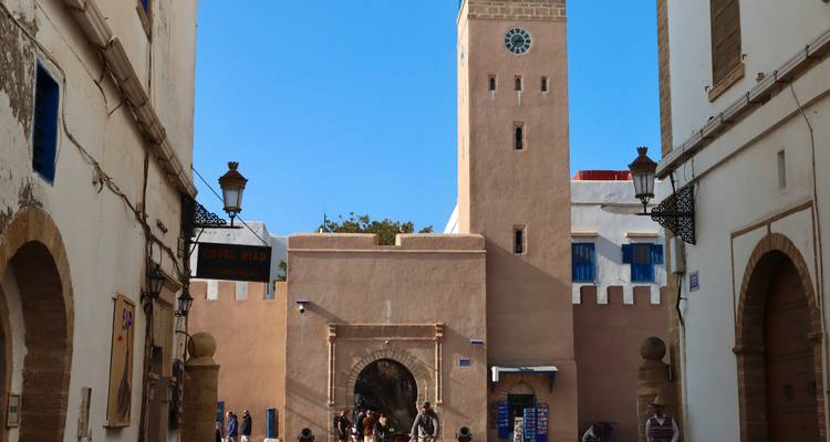 Calle estrecha de la medina enmarcada por la torre del reloj de color rosa arenoso y paredes encaladas en Essaouira