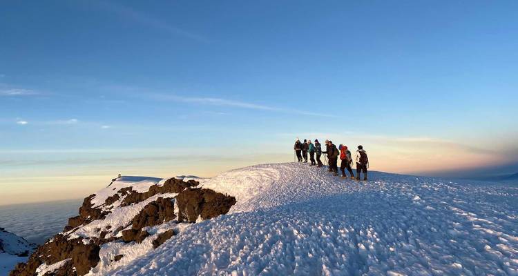 Gruppe steht auf einem schneebedeckten Gipfel während des Sonnenuntergangs.