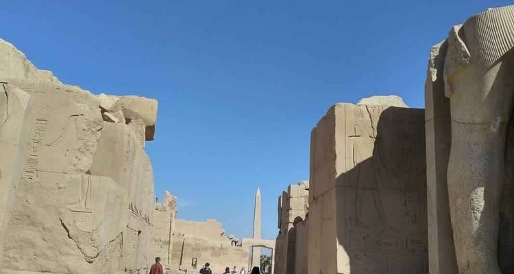 Ancient ruins with obelisk and people walking.