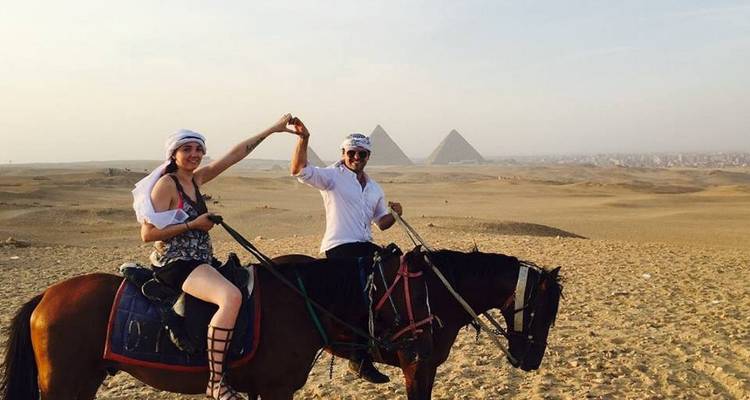 Pareja a caballo con pirámides al fondo.