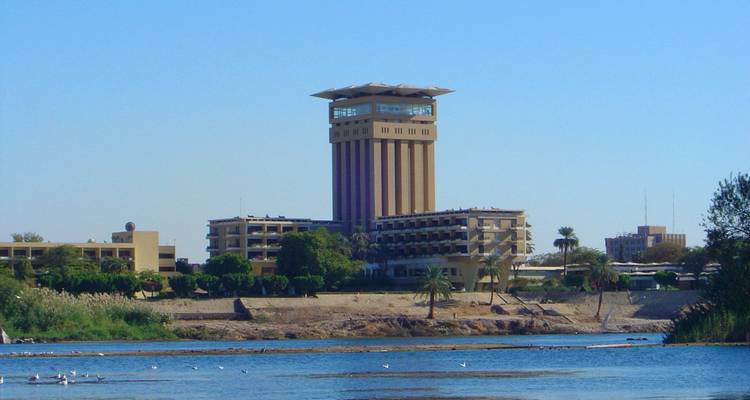 Torre hotelera moderna junto al río que se eleva sobre las orillas del Nilo bajo un cielo azul despejado.