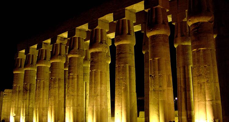 Fila de columnas altísimas en el Templo de Luxor iluminadas de forma dramática, brillando en dorado contra el cielo nocturno.