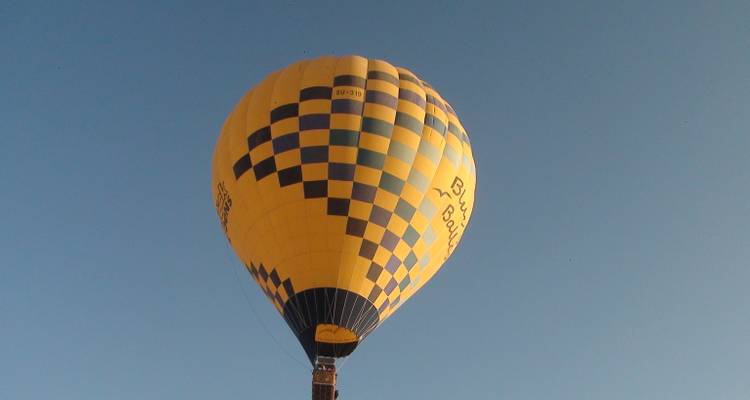Un globo aerostático amarillo y azul brillante ascendiendo hacia un cielo azul despejado.