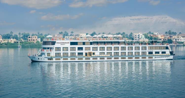 Cruise ship sailing on a calm river with a scenic backdrop.